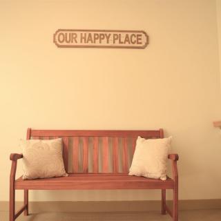 A cozy wooden bench with cushions sits beneath a wall sign reading 'OUR HAPPY PLACE'.