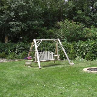 A peaceful garden scene featuring a bench swing set amidst a lush green lawn and surrounded by trees.