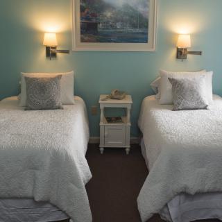A cozy bedroom featuring two twin beds with light bedding, a shared nightstand, and soft wall lighting.