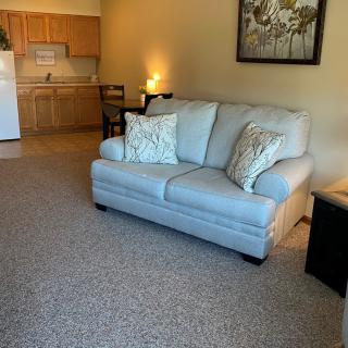 A cozy living room with a sofa and cushions, adjacent to a small kitchen area.