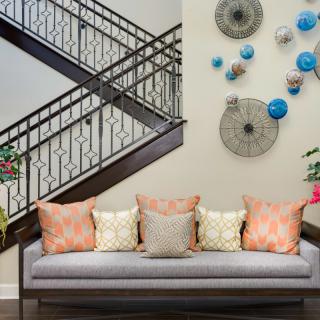 A stylish living room with a cozy sofa adorned with colorful pillows, and artistic wall decorations beside a modern staircase.