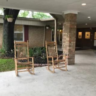 Two wooden rocking chairs on a covered porch with brick pillars and a garden view.