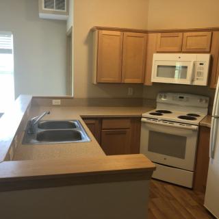 An empty apartment kitchen with wooden cabinets and standard appliances.