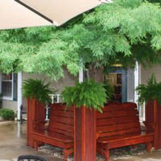 An outdoor patio with wooden seating and lush greenery under a large umbrella.