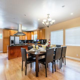 A modern dining area with a spacious kitchen, featuring a large table and chairs, illuminated by a chandelier.