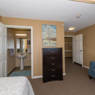 A cozy bedroom with a view into an adjacent bathroom, featuring a dresser and armchair.