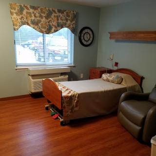 A clean and simple hospital patient room featuring a bed, chair, and window.
