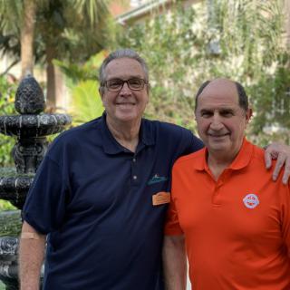 Two smiling men posing together outdoors in casual attire.