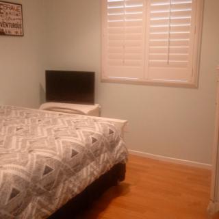 A small bedroom with a bed, television on a nightstand, and a window with shutters.