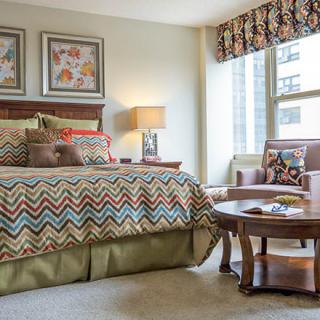 Cozy bedroom with a patterned bedspread, armchair, and window view.