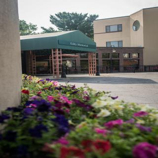 A building entrance with a green awning and colorful flowers in the foreground.