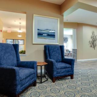 A cozy lobby area featuring two blue armchairs, a small side table, and framed artwork on the wall.