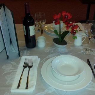 Elegant dining table setup with wine, plates, cutlery, and a flower centerpiece.