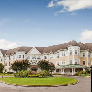 A grand hotel building with a circular driveway and well-maintained landscaping under a clear blue sky.