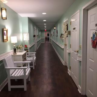 A long, warmly-lit hallway with doors on either side and chairs placed along the wall.