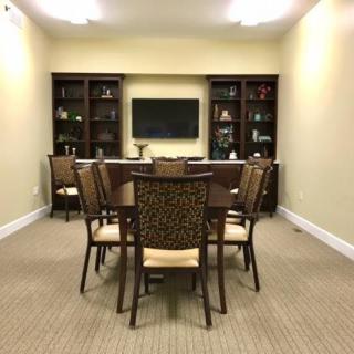 A well-organized conference room with a central table, surrounded by chairs, bookshelves in the back, and a television on the wall.