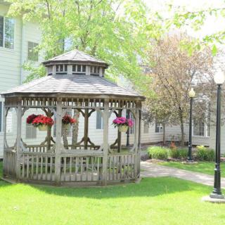 A charming wooden gazebo surrounded by a lush green lawn and colorful hanging flowers.