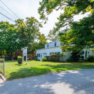 A suburban home surrounded by lush trees and a well-maintained yard, viewed from the driveway on a sunny day.