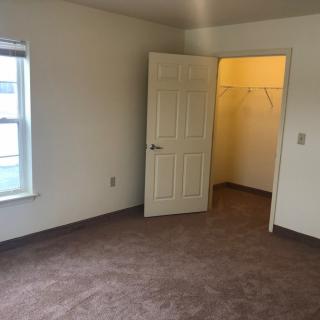 An empty room with carpet flooring, featuring an open door leading to a closet and a window.