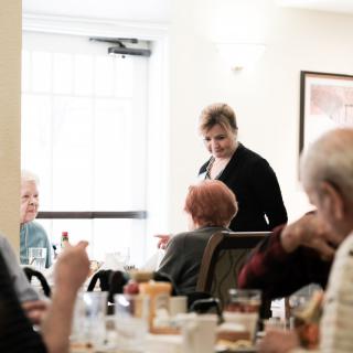Elderly individuals enjoying a meal and conversation in a dining setting.