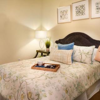 A cozy bedroom featuring a neatly made bed with decorative pillows and wall art, softly lit by a bedside lamp.