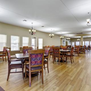 A spacious dining room with wooden floors and multiple tables and chairs arranged neatly under chandeliers.