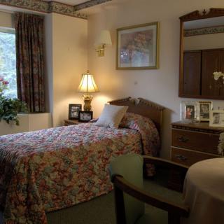 A cozy bedroom with a single bed, bedside lamp, dresser, and window with curtains.