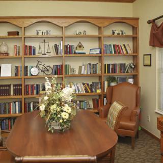 Cozy library reading room with a wooden table, bookshelves full of books, and a comfortable chair.