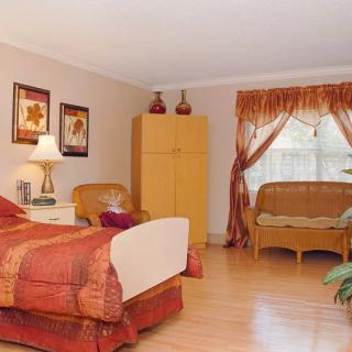 A cozy bedroom with a bed, armchair, wardrobe, and window seating area.