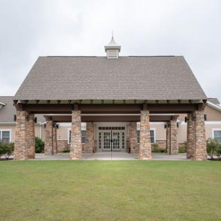 A stone-faced building with a large entrance supported by columns and surrounded by landscaped grass.