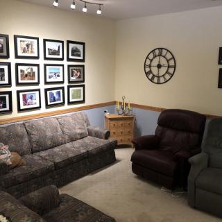 Cozy living room with multiple couches, armchair, wall clock, and photo gallery.