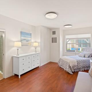 A bright and cozy bedroom with a bed, dresser, and ample lighting.