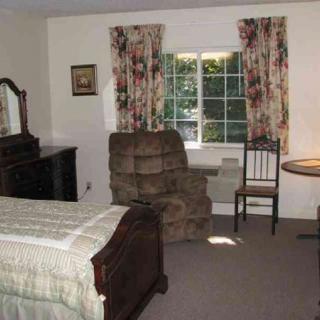 A cozy bedroom featuring a bed, armchair, table, and floral curtains.