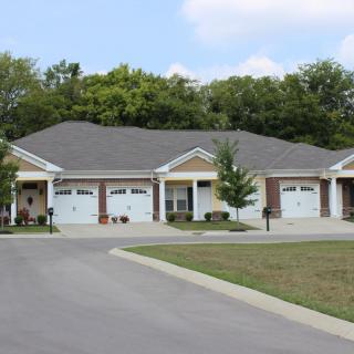 A row of suburban houses with garages and a driveway surrounded by trees.