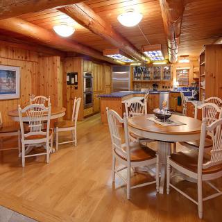 A cozy dining area with wooden interiors, featuring round tables and chairs adjacent to a kitchen.