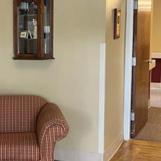 A cozy living room corner with a patterned sofa and a wall-mounted shelf beside an open doorway.