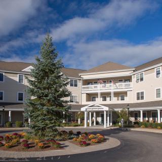 A large residential building with a central entrance, landscaped surroundings, and a partially cloudy sky.