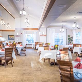 A spacious dining area featuring neatly arranged tables with white tablecloths, wooden chairs, and elegant chandeliers.