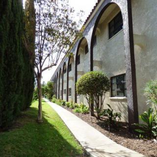 A pathway lined with trees and landscaping alongside a building featuring arches.