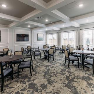 A modern dining room with multiple tables and chairs, featuring elegant lighting and a wall-mounted television.
