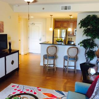 A cozy living room with a view into the kitchen, featuring bar stools and vibrant decor.