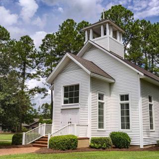 A quaint white church surrounded by trees under a clear sky.