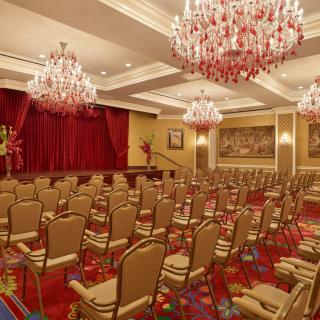 An elegant conference room with chandeliers and arranged seating facing a stage.