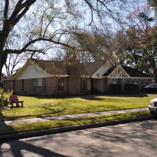 A suburban house with a well-kept lawn and trees on a sunny day.