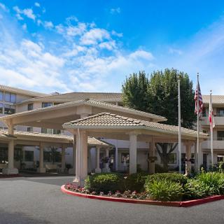 A large building with a covered entrance, surrounded by landscaping and flags, under a clear blue sky.