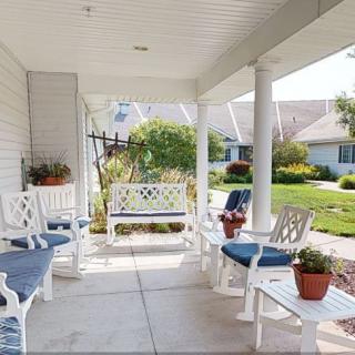 A cozy porch with white furniture, decorative pillows, and potted plants overlooking a garden.