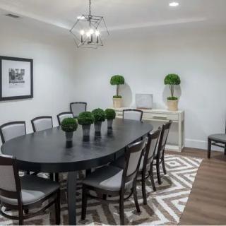 A modern dining room with a black oval table, surrounded by chairs and decorated with green plants and wall art.