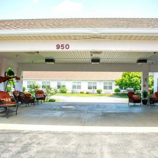 A covered entrance with seating areas leading to a building surrounded by greenery.