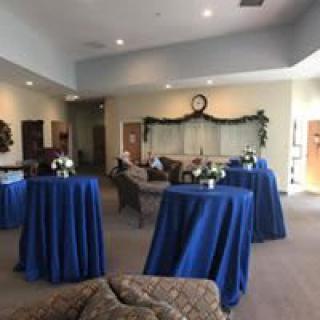 A reception area with blue tablecloths and floral arrangements on high tables.