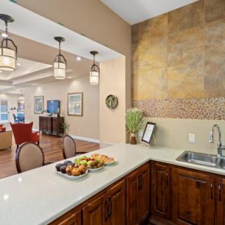 A modern kitchen with a light-colored countertop, featuring a fruit plate and sink, connected to an open-concept living area.